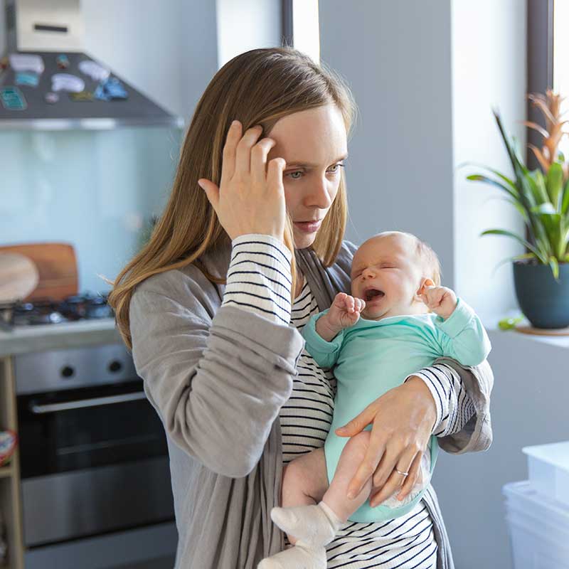 Erschöpft wirkende Mutter hält ihr Baby